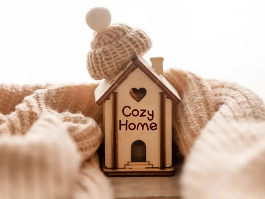 Small wooden Cozy Home house wrapped in a knitted blanket and hat