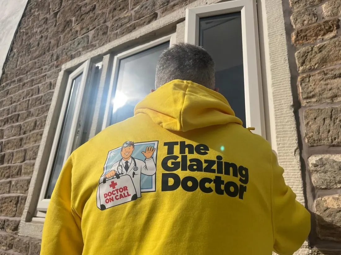 Glazing Doctor fitter in a branded yellow hoodie checking a window